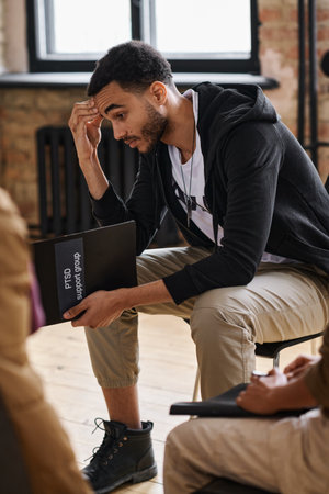 Young sad man with post traumatic syndrome sitting among other people with similar problems while...