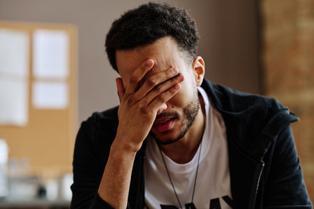 Young depressed man touching face while suffering from post traumatic syndrome and describing his problems at psychological sessionの写真素材