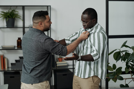 Young violent Hispanic man menacing to his African American colleague while attacking him and saying something offensiveの写真素材