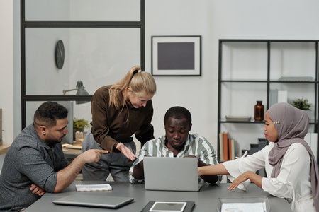 Group of intercultural displeased employees bullying African American male colleague sitting by...