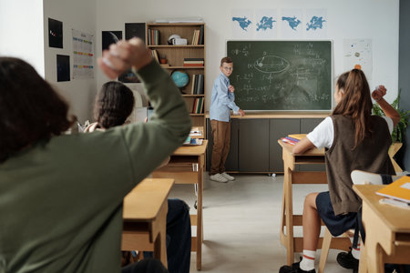 Cute schoolboy standing by blackboard with written formulas while classmates throwing crumpled paper at him at lessonの写真素材