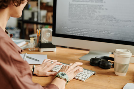 Hands of young female programmer typing on computer keyboard while decoding data on computer screen...