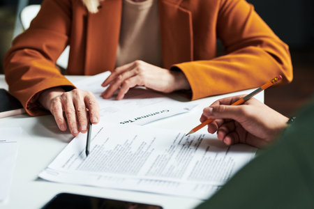 Hand of mature teacher of foreign languages pointing at one of documents while explaining...