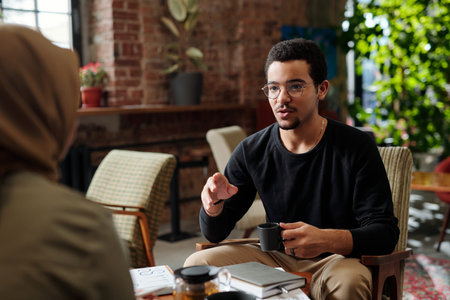 Young confident multi-ethnic businessman in casualwear explaining something to Muslim female...