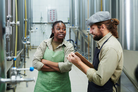 Brewery worker talking to manager when they are standing among tanks with fermenting drinksの写真素材