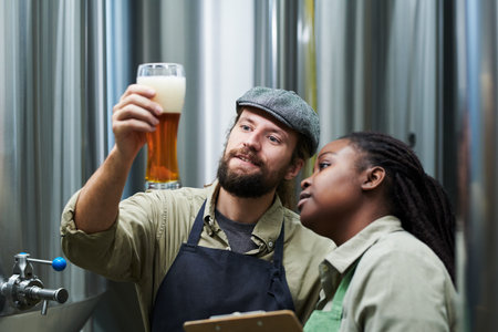 Smiling brewery workers checking thickness of beer frothの写真素材