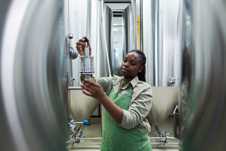 Black woman working at craft beer factory, checking brewing equipment