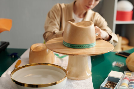 Close-up of wooden workpiece in form of hat against young craftswoman measuring circumference while creating new items for saleの写真素材