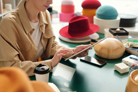 Close-up of young creative female entrepreneur using tablet while sitting by workplace and looking...