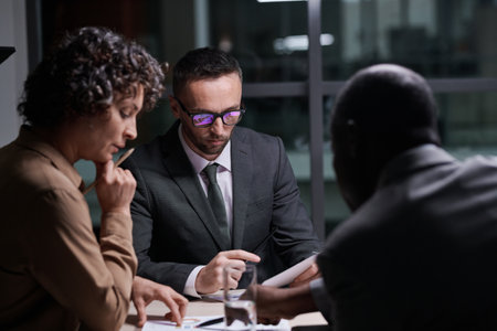 Focus on serious broker analyzing financial document in front of two intercultural colleagues...