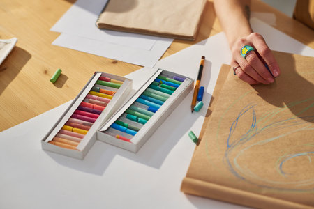 Close-up of hand of young creative female artist sketching on paper or notepad with blue crayon...