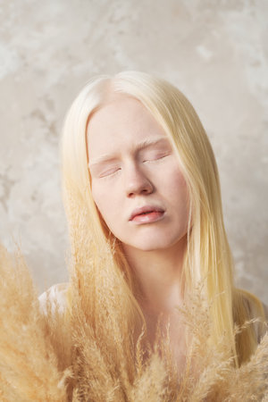 Close-up portrait of young serene albino woman with fluffy dried flowers keeping eyes closed while standing in front of camera in isolationの写真素材