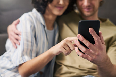 Selective focus on hands of young couple with smartphone choosing food for lunch in online menu while relaxing at home on weekendの写真素材