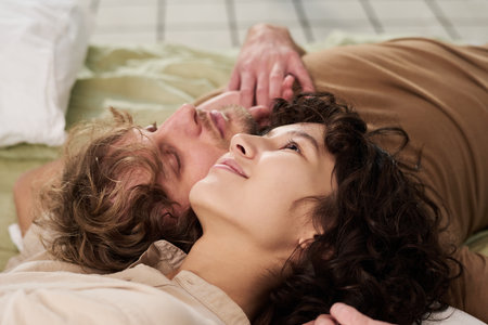 Close-up of happy young romantic couple touching by their heads while relaxing on bed after sleep in the morning and enjoying restの写真素材