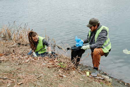 Young people in neon vests collecting plastic bags and bottles in trash bags when cleaning lake...