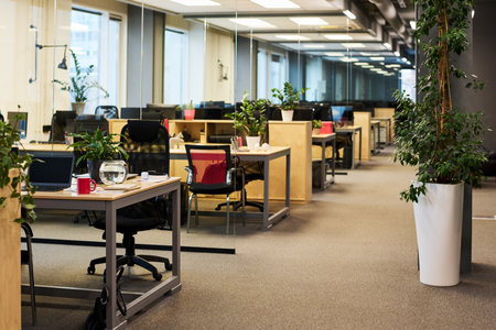 Spacious office with large number of green plants growing in flowerpots and on desks with armchairs...