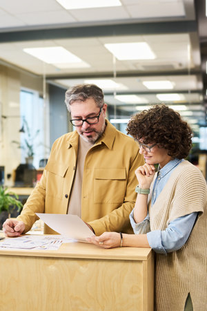 Two economists looking at financial paper with charts, analyzing data and discussing it while...