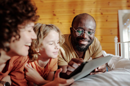 Smiling African American man pointing at tablet screen while showing his little son something curious in online video during home restの写真素材