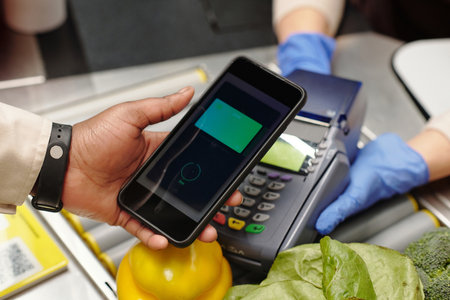 Close-up of consumer hand holding smartphone over card reader during contactless payment for food products in supermarketの写真素材