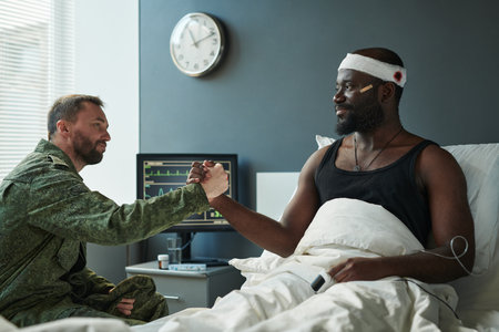 Young African American soldier with wounded head and his friend handshaking during communication in...