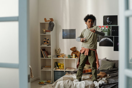 Cute active schoolboy standing on double bed and training defense exercise while practicing karate or some other martial artの写真素材