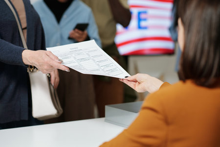 Close-up of young woman from electoral commission passing ballot paper to one of voters standing in queue in front of registration deskの写真素材