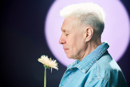 Side view of senior man looking at flower blooming at night and feeling its smell while standing against full moon and dark skyの写真素材