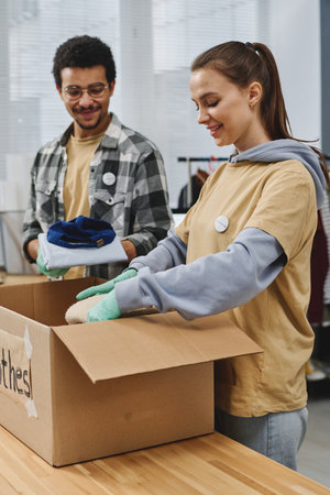 Young intercultural volunteers preparing free clothes for people in need and packing them in big box in office of volunteering organizationの写真素材