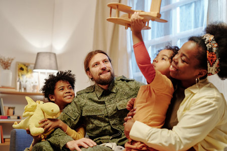 Affectionate intercultural family of four spending time together at home while mother embracing younger son playing with toy airplaneの写真素材