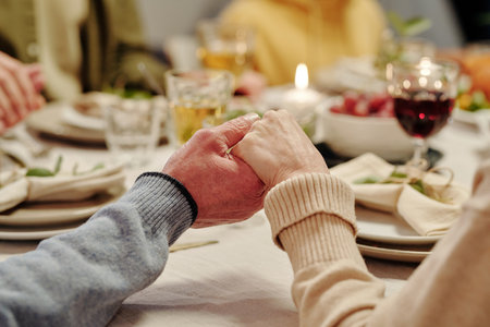 Hands of affectionate senior couple praying by served festive table with homemade food and burning candles before Thanksgiving dinnerの写真素材