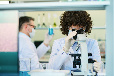 Brunette female scientist sitting by workplace in front of camera and studying new virus in...
