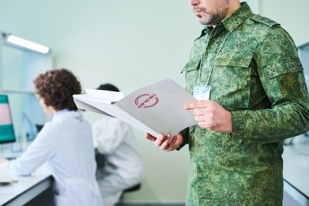 Mature officer in camouflage uniform looking through documents containing secret information describing military experimentの写真素材