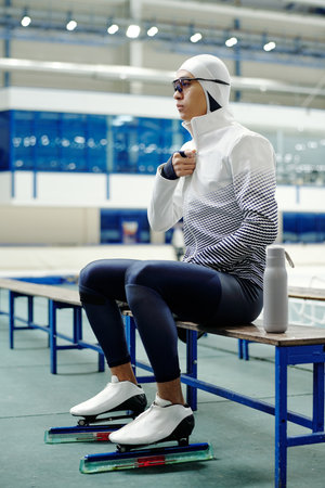 Young short track speed skating athlete in uniform and skaters sitting on bench and having minute of...