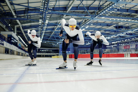 Young male ice skater in sports uniform and two more sportsmen behind him sliding forwards along rink while taking part in competitionの写真素材