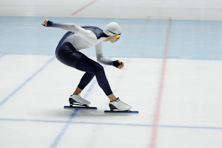 Young speed skater bending forwards over ice rink while standing or moving along arena during race or practice of new exercisesの写真素材
