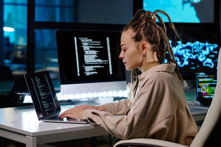 Young IT engineer sitting in armchair by workplace in dark office and working over decoding new data...