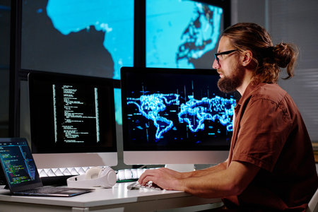 Side view of young serious male programmer decoding data on computer screen and typing on keyboard while using new softwareの写真素材