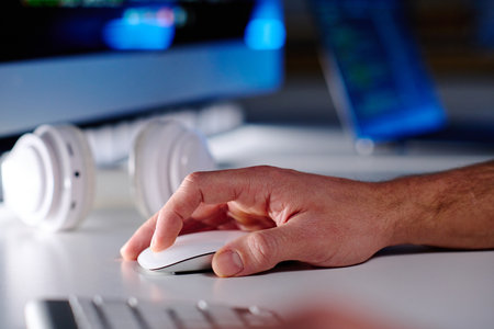 Hand of mature male IT manager clicking mouse while sitting by workplace in front of computer in office and networking or decoding dataの写真素材