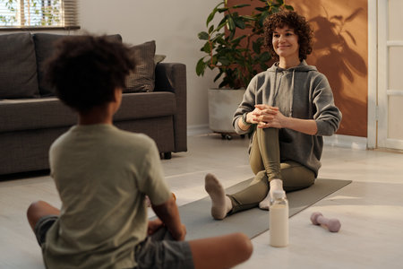 Focus on happy young mother practicing exercise on mat in front of her son during home workout and explaining him how to do itの写真素材