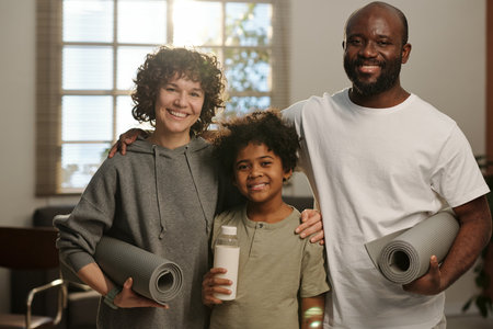Happy young intercultural family of father, mother and son standing in front of camera and looking at you after morning workoutの写真素材