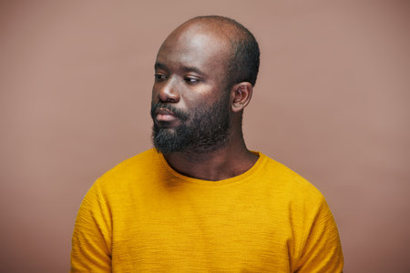 Portrait of African American man in yellow shirt looking away with sad expression on brown backgroundの写真素材
