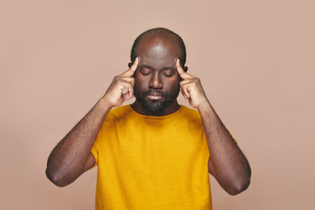 African American man contemplating about new idea holding his head with hands standing against brown backgroundの写真素材