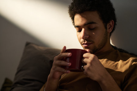 Young man in melancholy enjoying hot coffee and thinking about his life momentsの写真素材