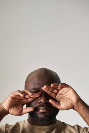 Vertical image of depressed man closing his eyes with hands against white backgroundの写真素材