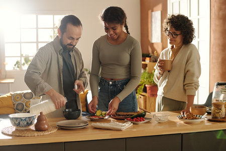 Parents with adopted daughter preparing sandwiches for breakfast together standing in the kitchen