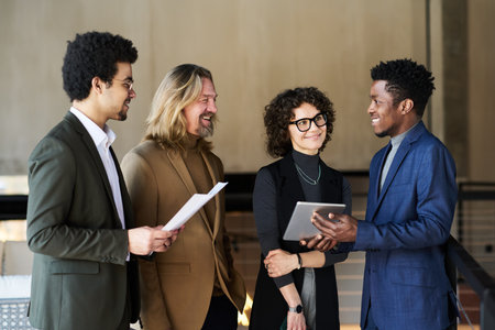 Group of happy brokers listening to young African American colleague with tablet making presentation of stock market fluctuationsの写真素材