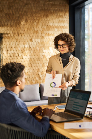 Confident businesswoman pointing at circle diagram on paper document while explaining graphic data...