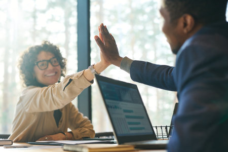 Focus on hands of two young intercultural successful colleagues giving each other high-five while...
