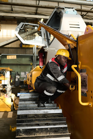 Young repairman in workwear and protective helmet checking condition of engine of huge industrial...