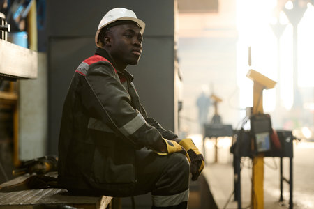 Young tired African American workman sitting on metallic bench while resting at break in the middle...